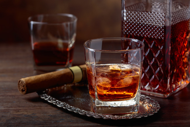 Glass of whiskey with natural ice and cigar on old wooden table.