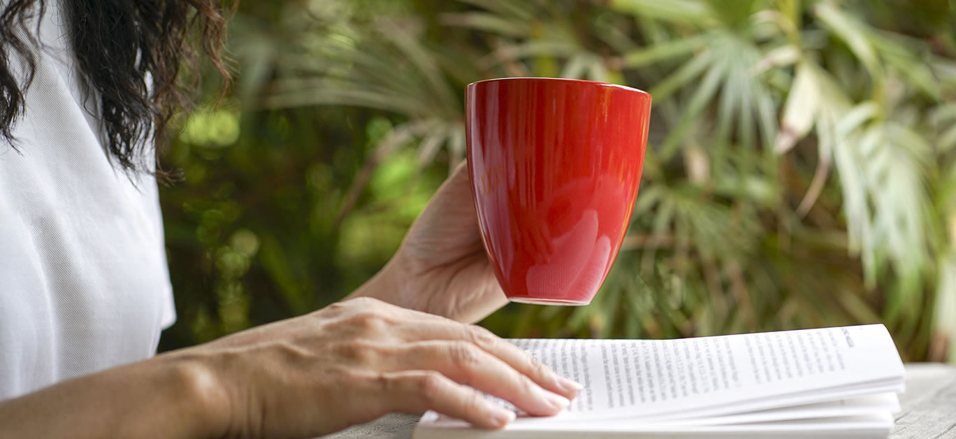 Woman having a cup of coffee and reading a book, close up