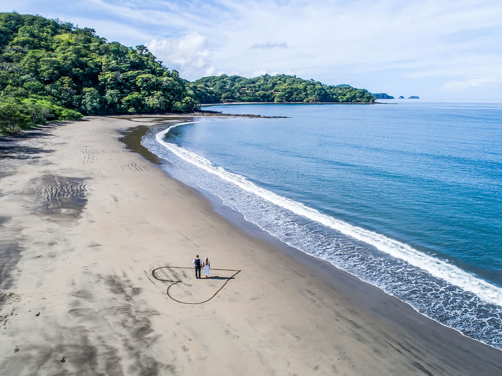 Aerial shot of wedding dress couple on the tropical beach Playa Arenillas in Costa Rica with a heart drawn into Sand