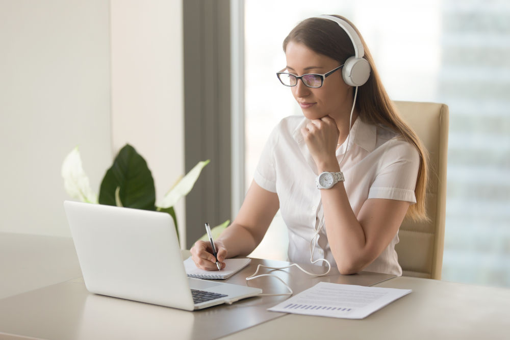 Focused attentive woman in headphones sits at desk with laptop