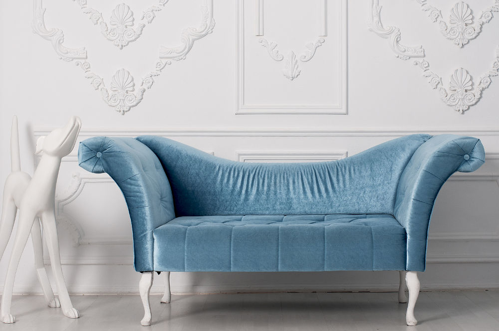 luxurious blue velvet sofa and and white sculpture of a dog near the armrest behind a white wall