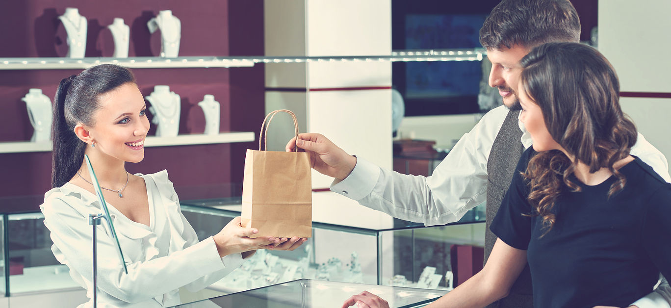 Service at the shop. Beautiful happy loving couple receiving their purchase in a shopping bag from a professional jeweler shop store assistance job love anniversary spending customers handing giving