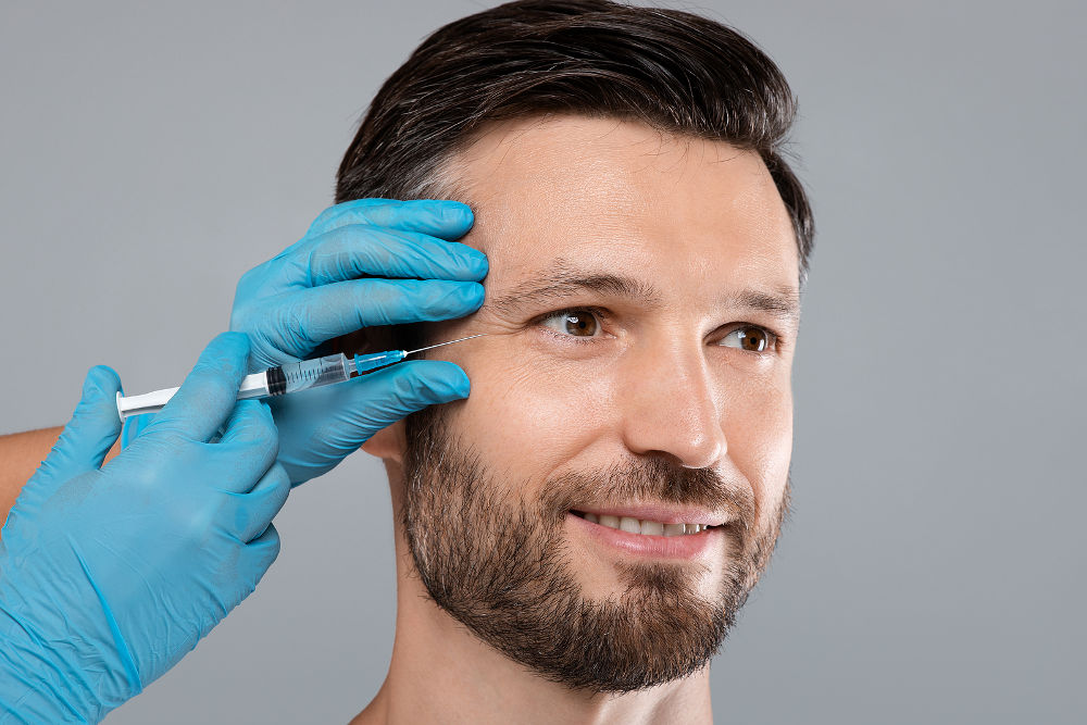 Closeup of happy handsome bearded man getting under eye injection