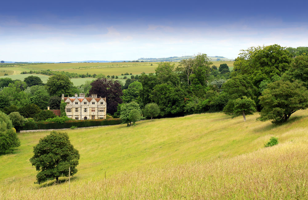 Landscape format image of a country manor looking across an open rolling field to the foreground. Located in rural Wiltshire UK in a small village called Wishord Cum lake.