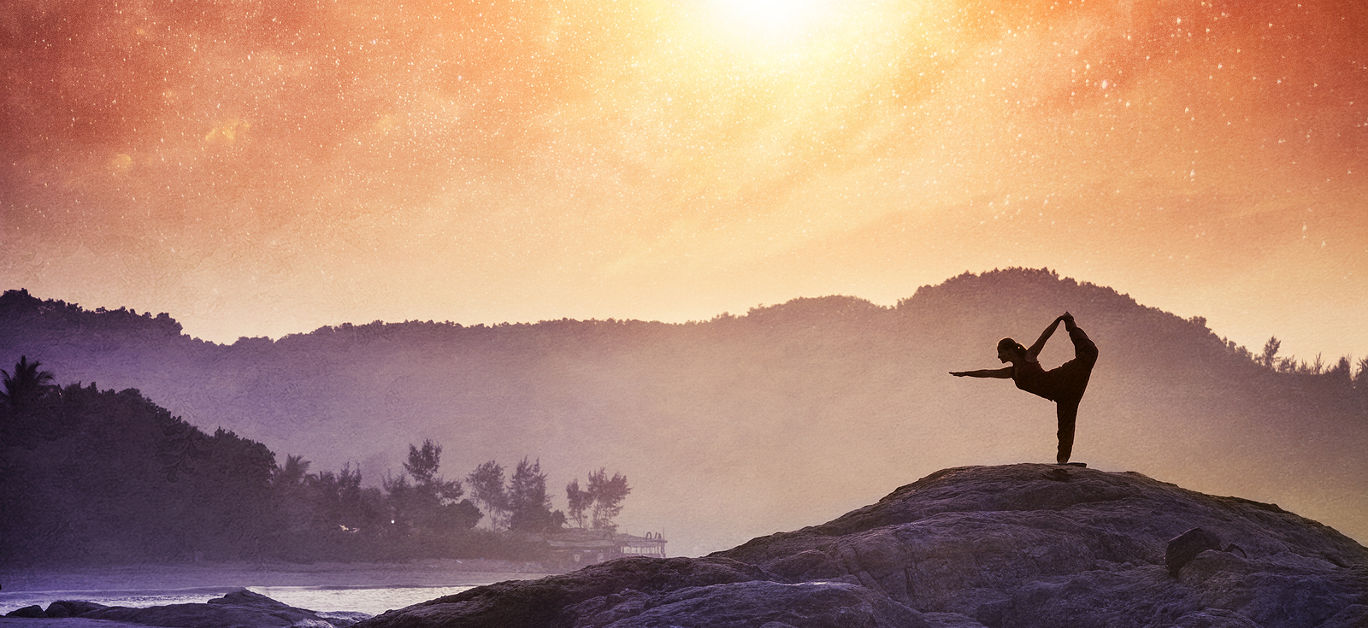 Woman doing Yoga natarajasana dancer pose on the rocks at sunset at Om beach Gokarna India