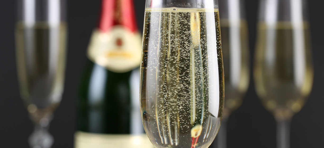 Champagne with bubbles in a glass with a bottle and more glasses in the background