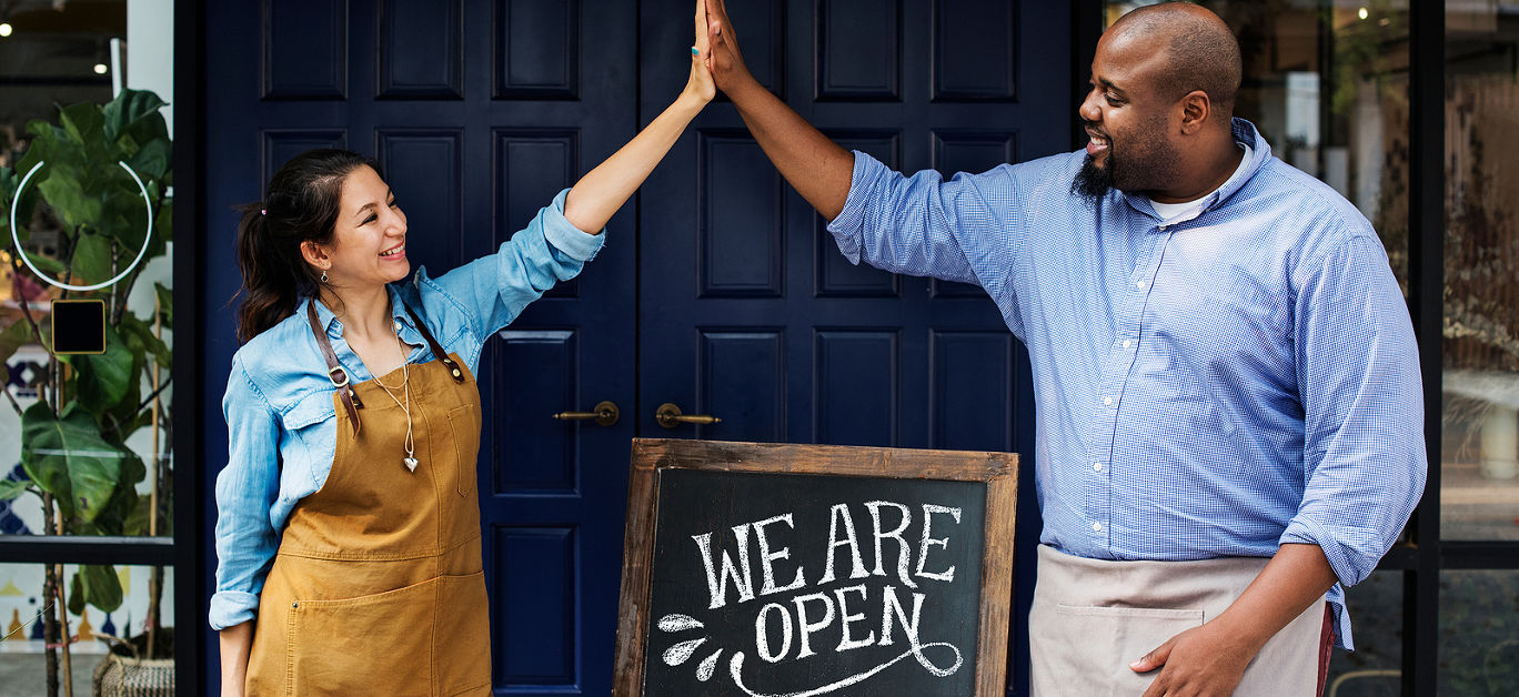 Cheerful business owners standing with open blackboard