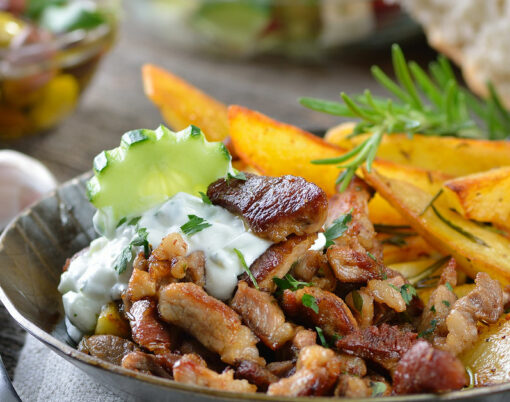 Greek pork gyros in an iron pan, served with tzatziki and fried potatoes, pitabread, salad and olives