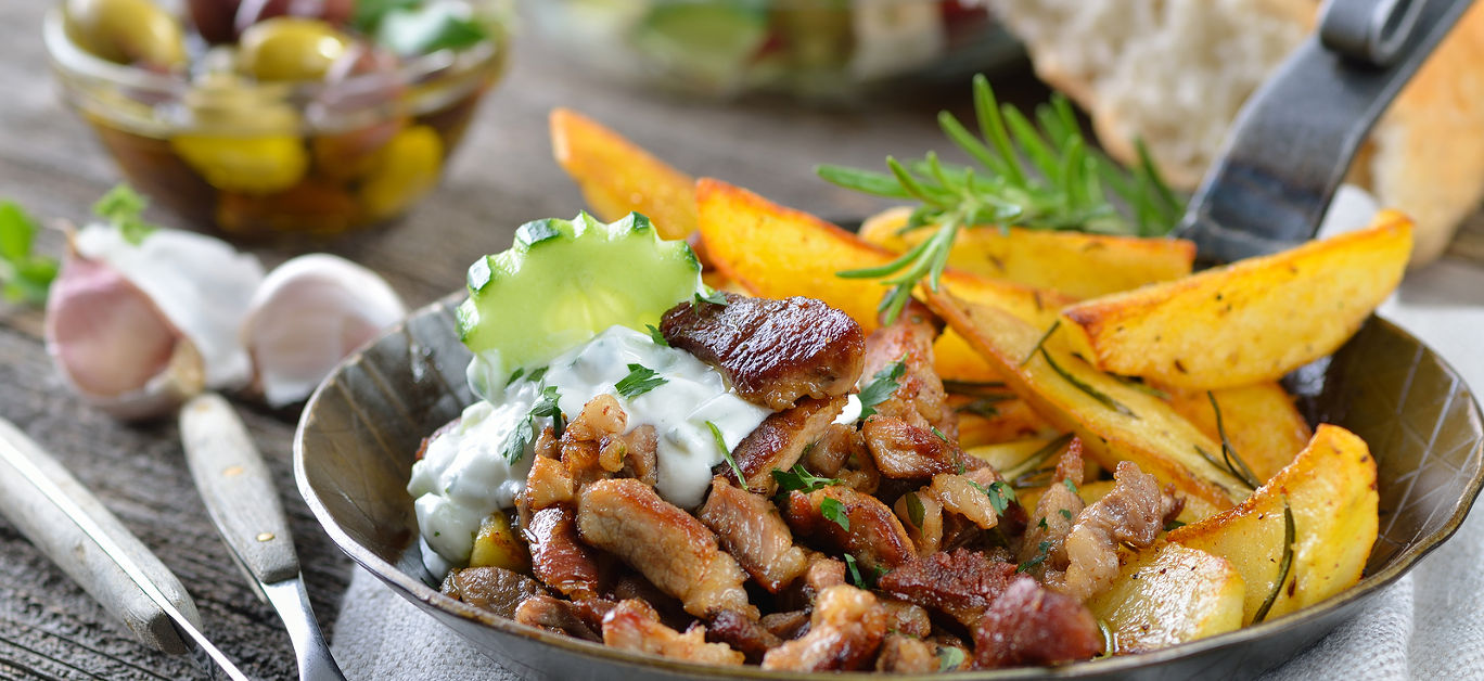 Greek pork gyros in an iron pan, served with tzatziki and fried potatoes, pitabread, salad and olives