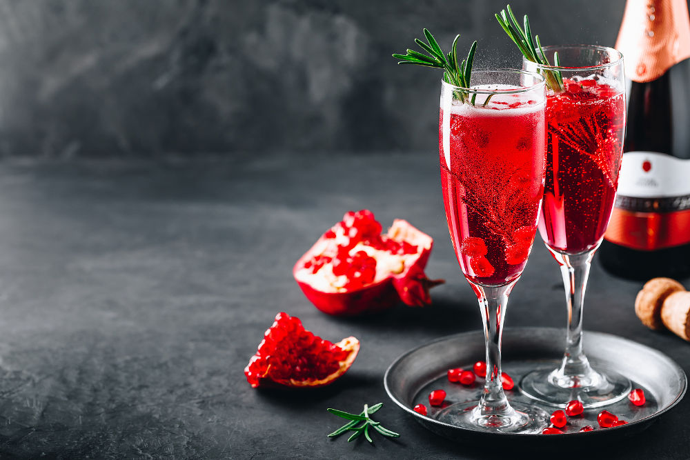 Pomegranate Champagne Cocktail with rosemary on gray concrete stone background, copy space