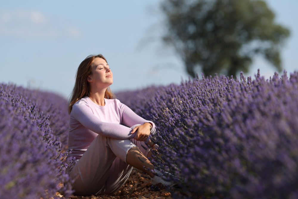 Relaxed woman breathing fresh air sitting in a lavender field a sunny day