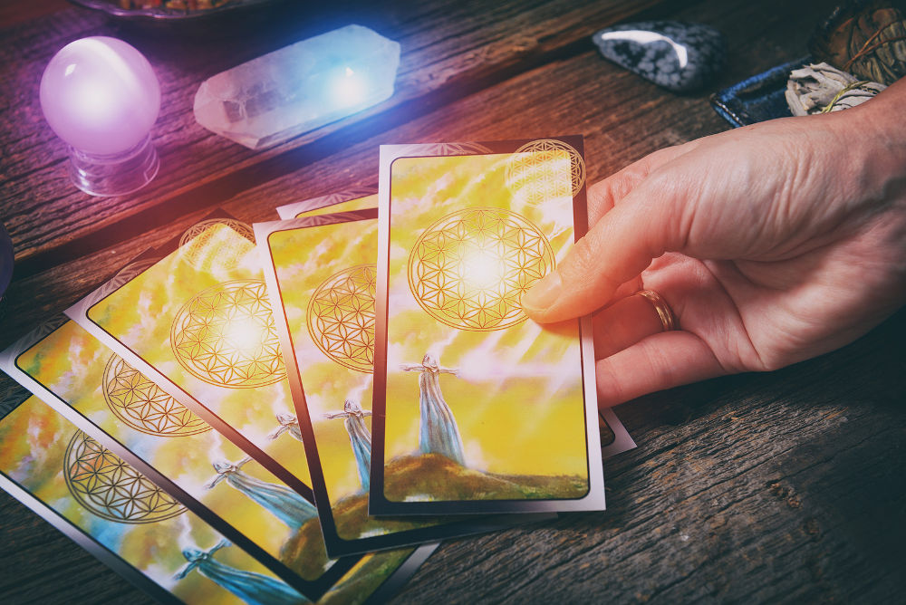 Tarot cards in hand, dowsing tool and crystals on a wooden board