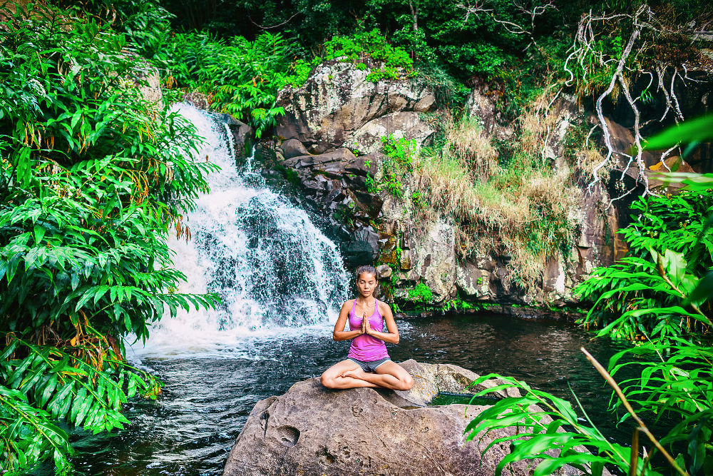 Yoga retreat woman praying doing the lotus pose meditating at waterfall forest in Kauai, Hawaii.