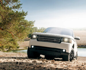 Car Land Rover Range Rover stand on sand near lake and forest at daytime