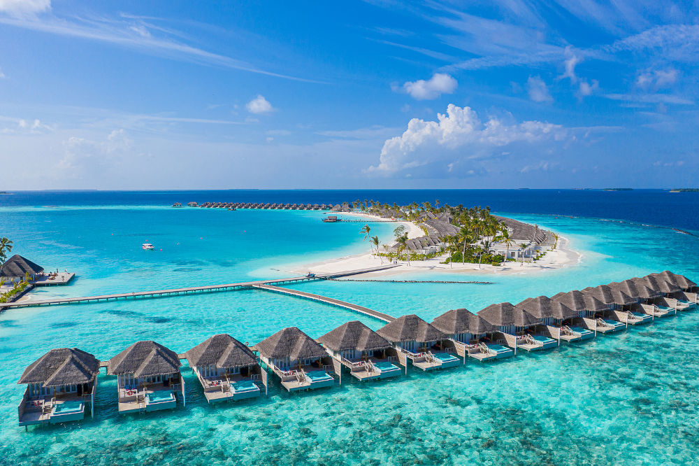 Aerial view of Maldives island, luxury water villas resort and wooden pier. Stunning sky and ocean lagoon beach. Summer vacation holiday and travel concept. Paradise aerial landscape panorama