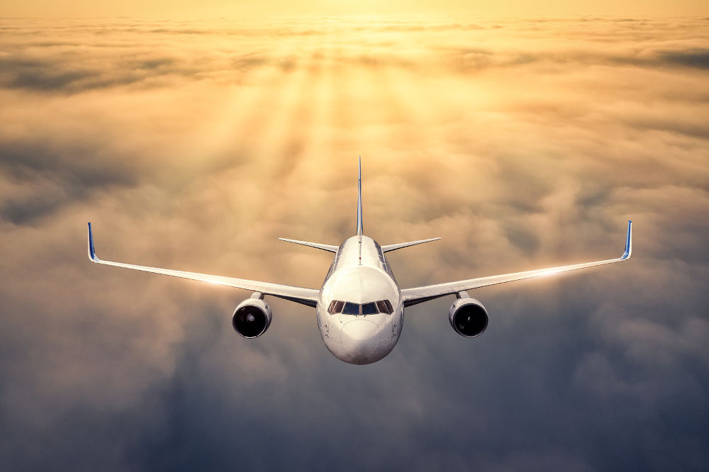 Airplane is flying above the clouds at sunset in summer.