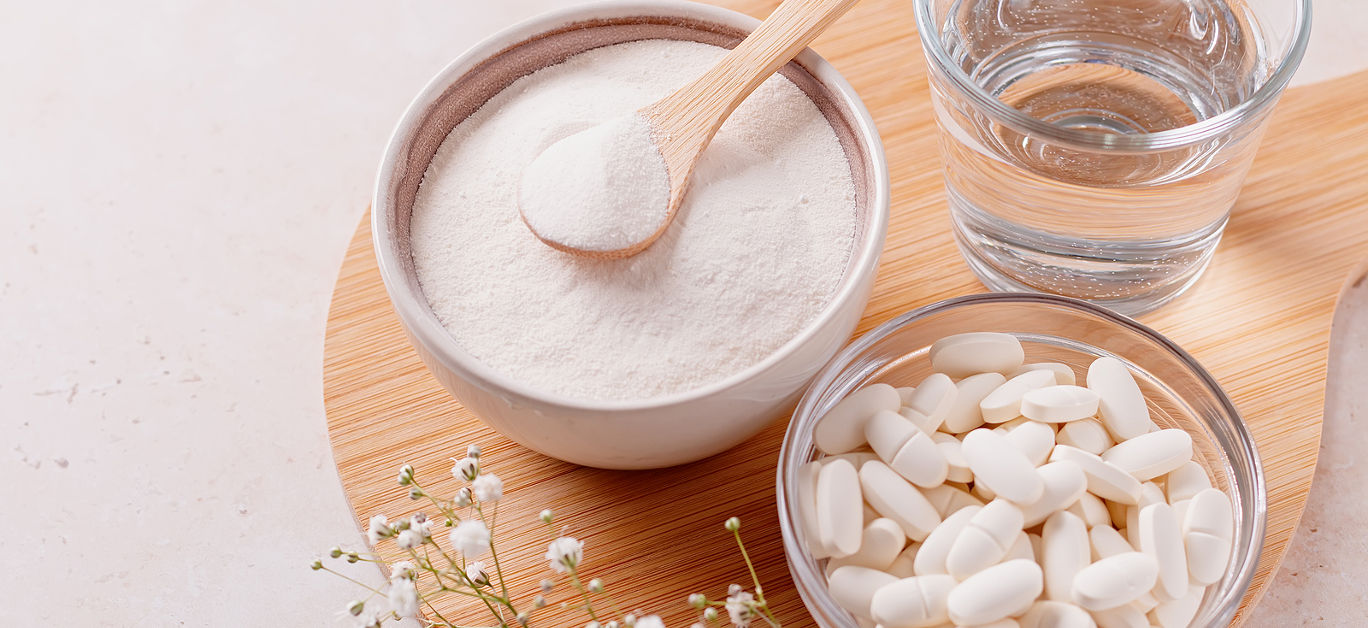 Collagen powder, pills and glass of water on wooden tray, top view