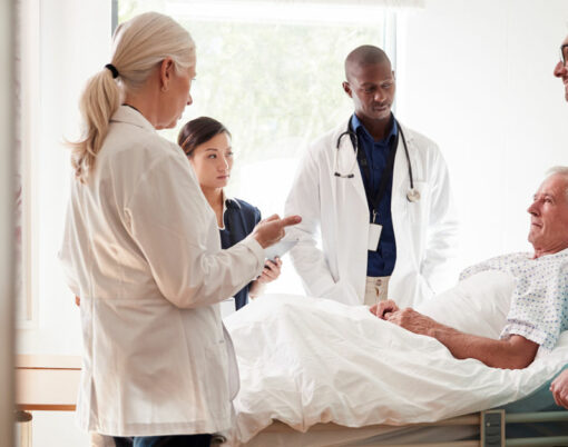 Medical Team On Rounds Meeting Around Bed Of Senior Male Patient