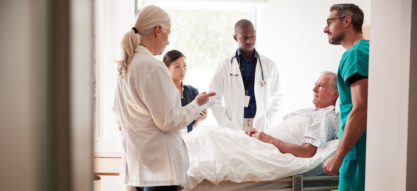 Medical Team On Rounds Meeting Around Bed Of Senior Male Patient