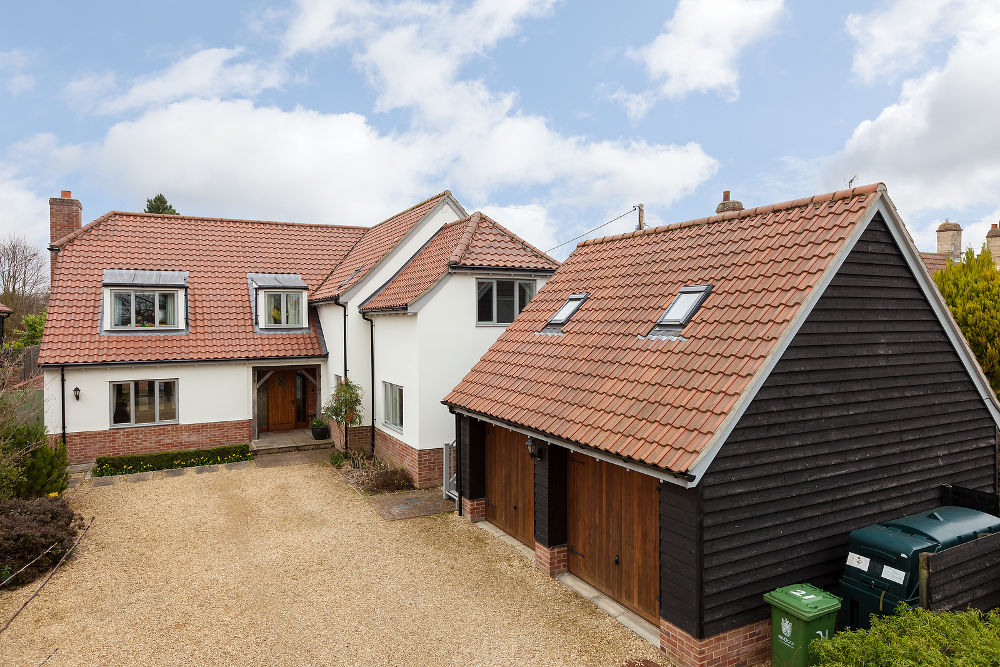 Brick and render luxury detached village house with double timber clad garage viewed from the public highway