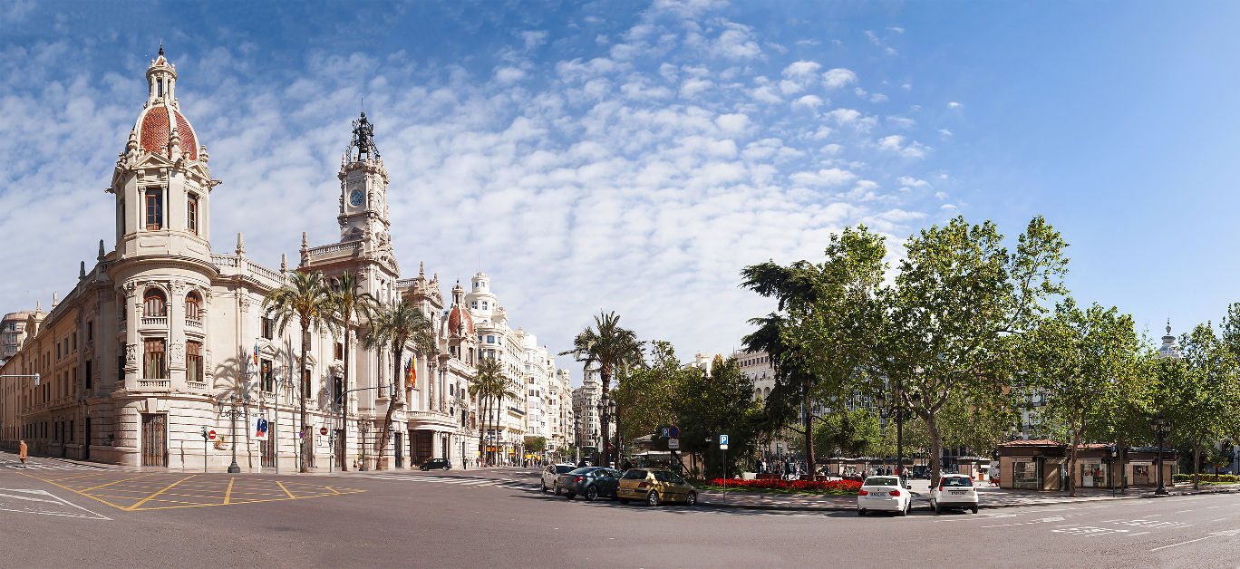 Town square (Plaza del Ayuntamiento) with palm trees and parked cars on a sunny day in Valencia, Spain