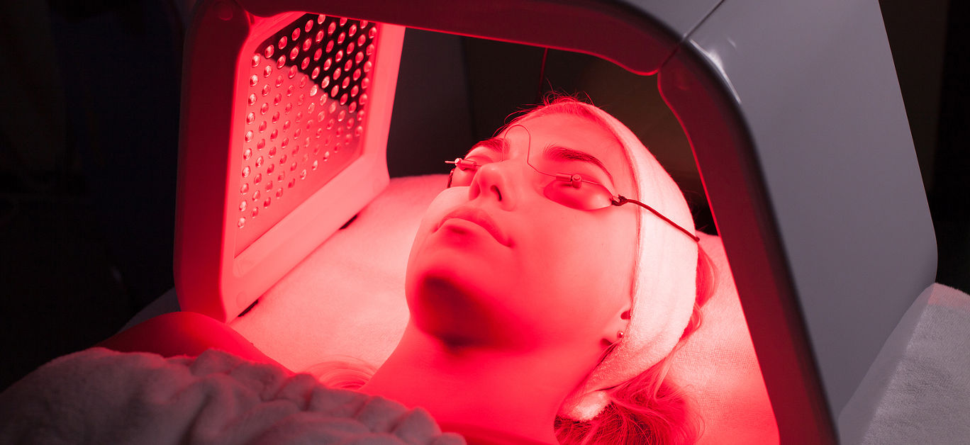 Young woman having LED light facial treatment in beauty salon