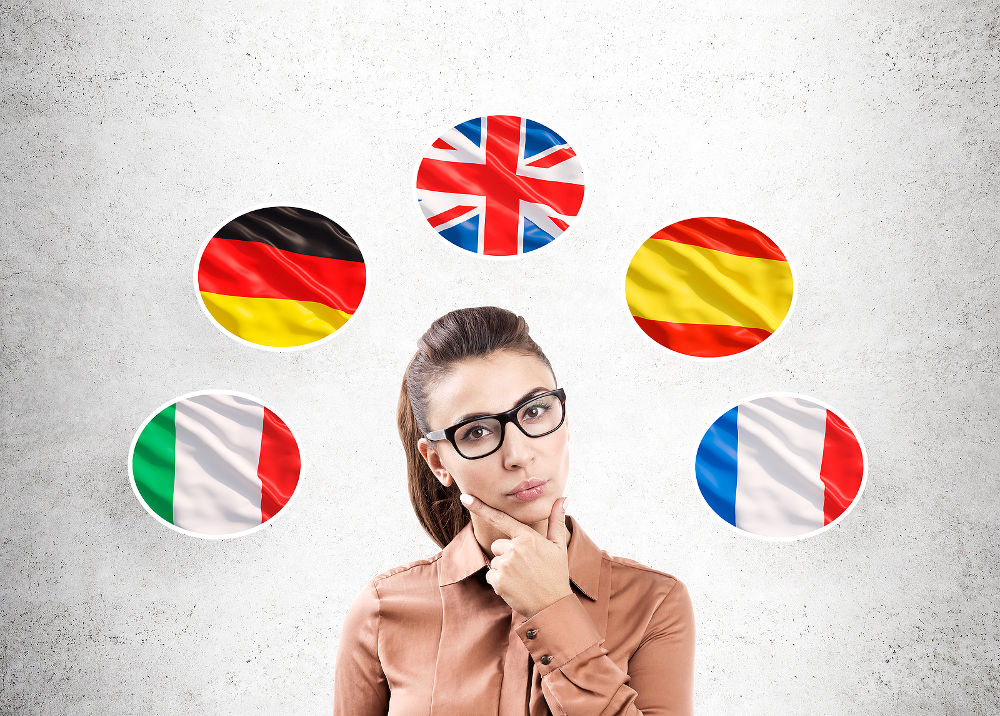 Portrait of a pensive woman in brown clothes standing near a gray wall with and five national flags around her.