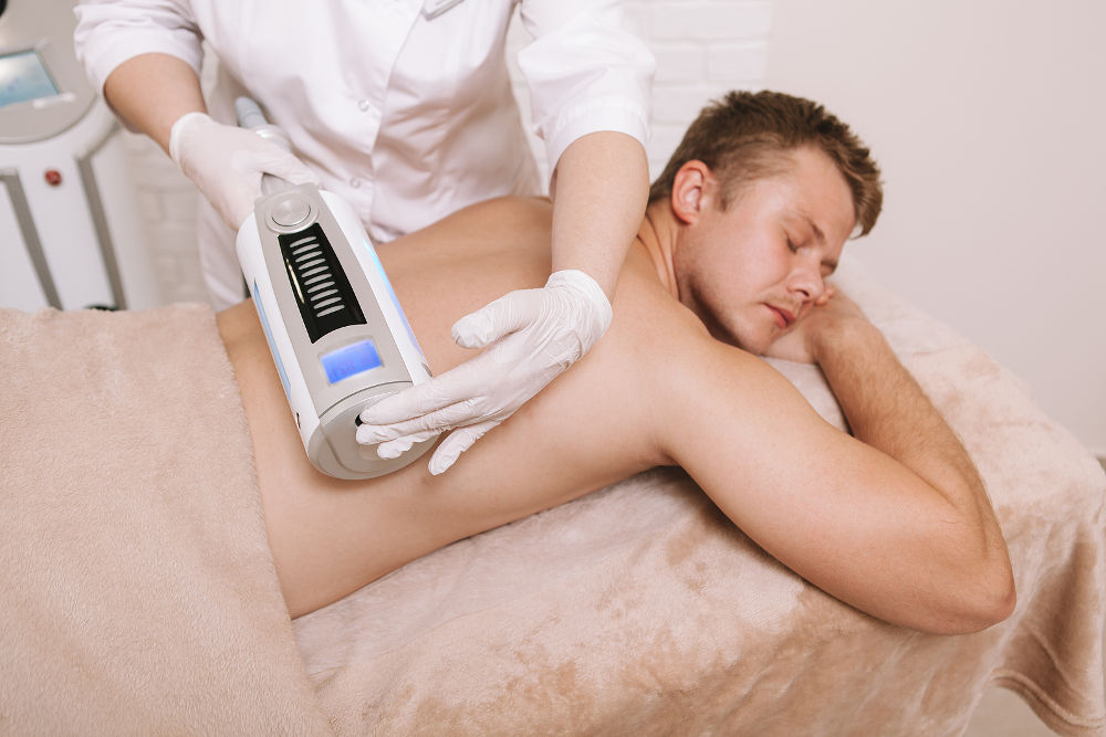 Male patient receiving endospheres massage at beauty clinic. Cosmetologist massaging back of a client using endospheres device