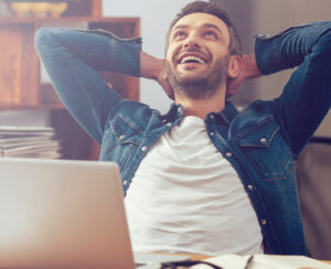 Happy young man working on laptop while sitting at his working place in office