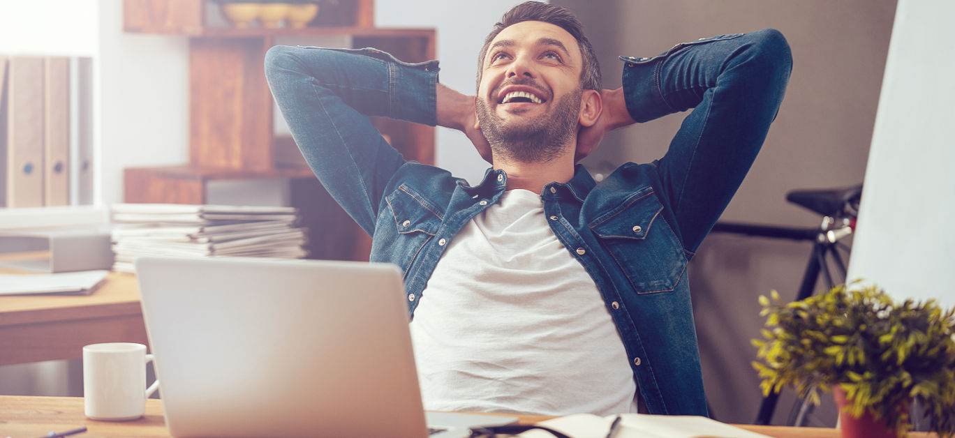 Happy young man working on laptop while sitting at his working place in office