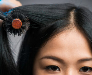 Cropped image of a hairstylist drying the hair of the customer at the beauty salon isolated on grey