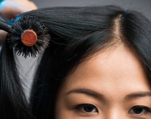 Cropped image of a hairstylist drying the hair of the customer at the beauty salon isolated on grey