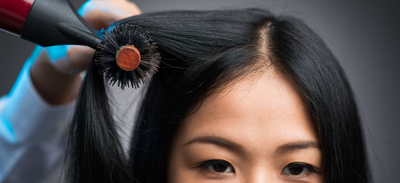 Cropped image of a hairstylist drying the hair of the customer at the beauty salon isolated on grey