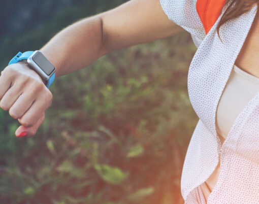 Woman looking at smart watches on her wrist, while trekking and walking along mountain meadows, outdoors