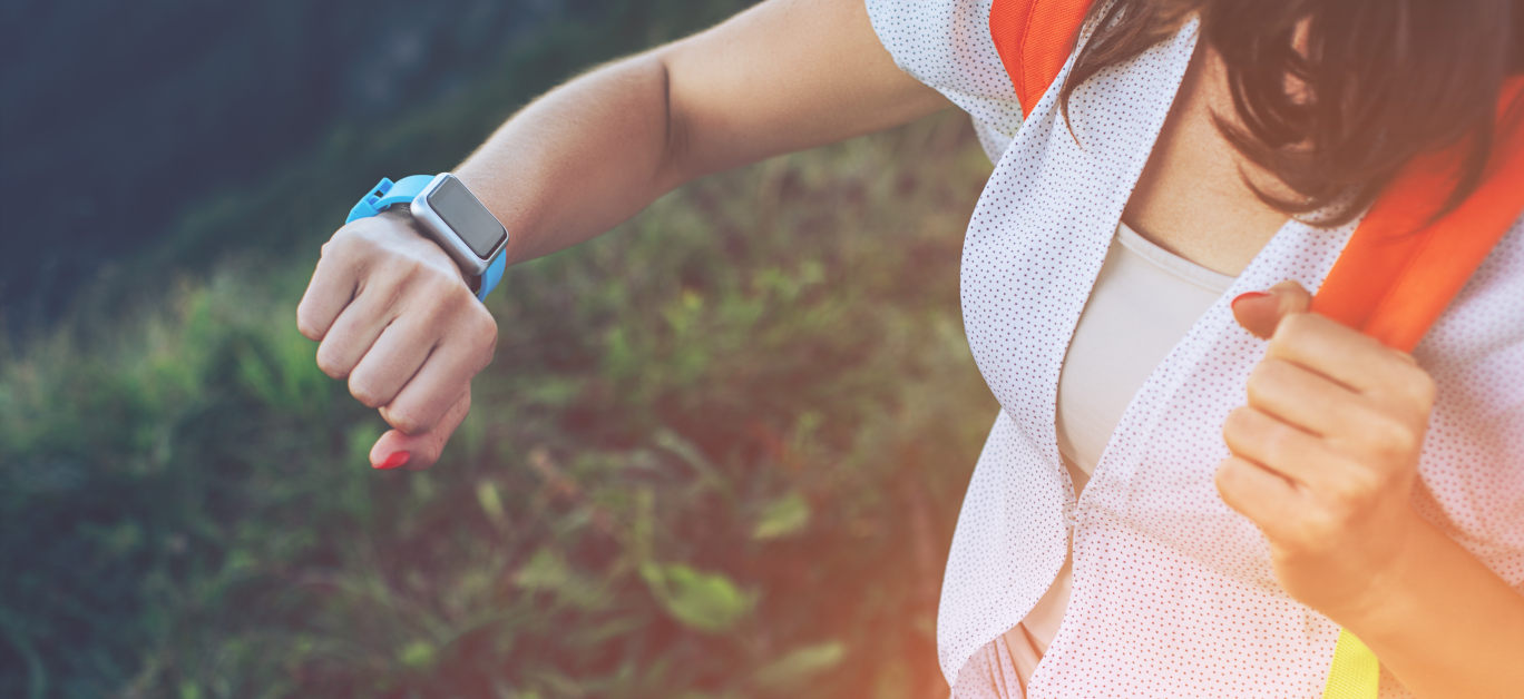 Woman looking at smart watches on her wrist, while trekking and walking along mountain meadows, outdoors