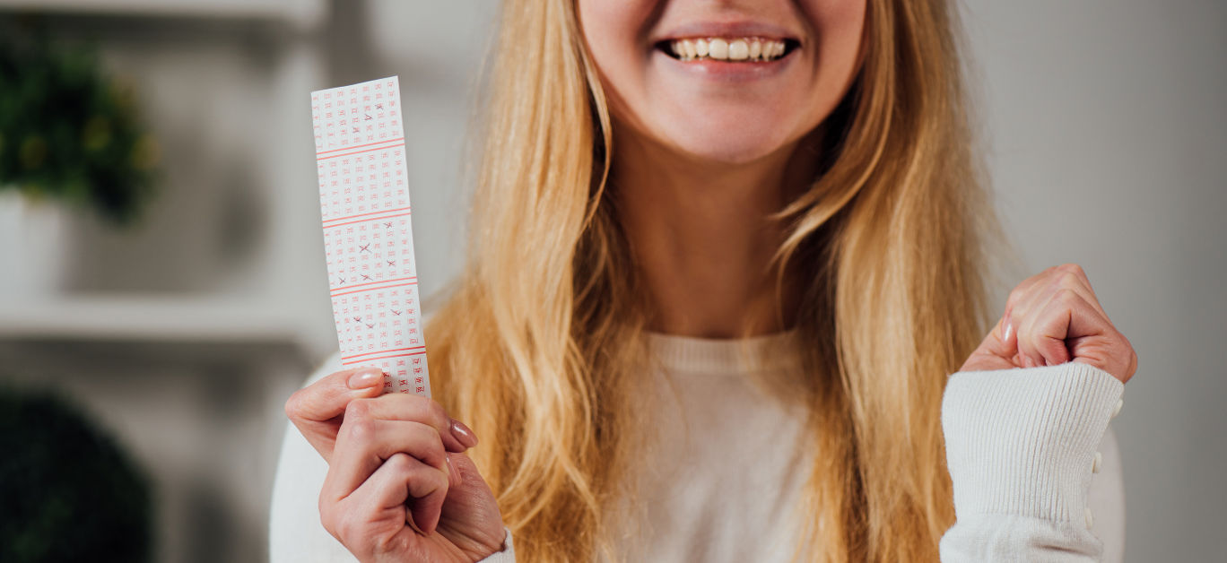 cropped view of woman showing winner gesture while holding lottery ticket