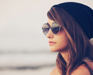 Fashion portrait of young hipster woman with hat and sunglasses on the beach at sunset, retro style color tones