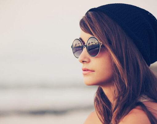 Fashion portrait of young hipster woman with hat and sunglasses on the beach at sunset, retro style color tones