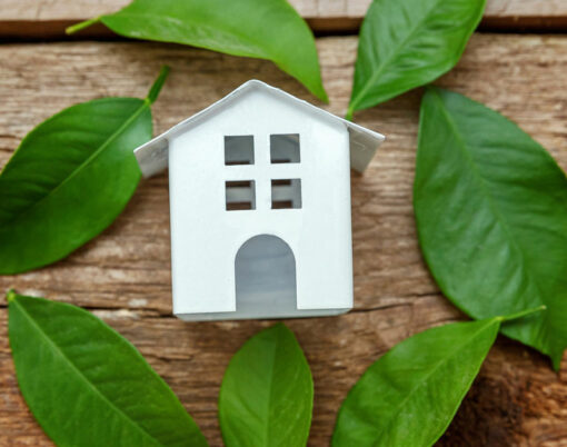 Miniature white toy model house with green leaves on wooden backgdrop