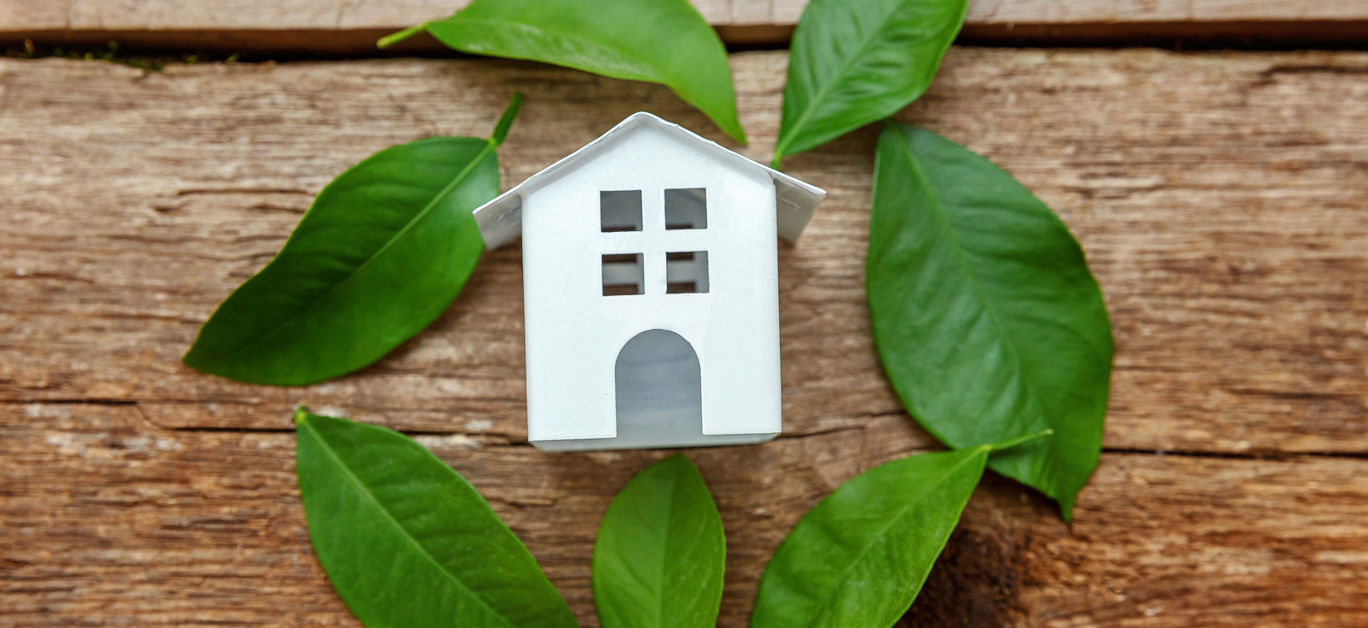 Miniature white toy model house with green leaves on wooden backgdrop