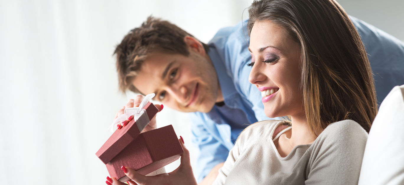 Young woman receiving a surprise gift box from her boyfriend at home.