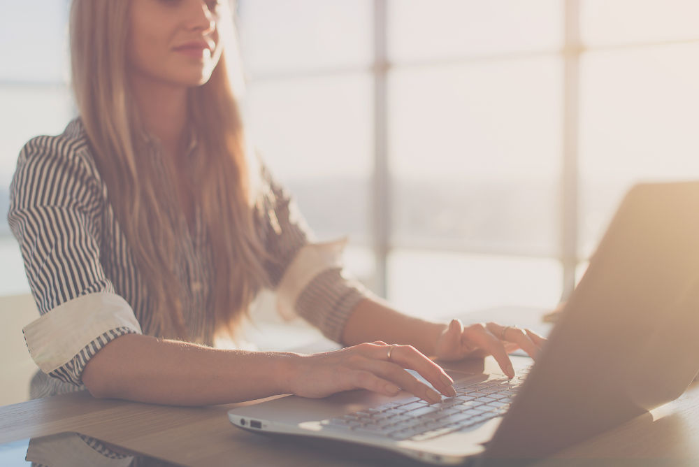 Female writer typing using laptop keyboard at her workplace in the morning