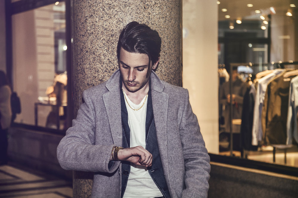 Elegant attractive young man outdoor wearing wool coat, in European city, looking at wrist watch