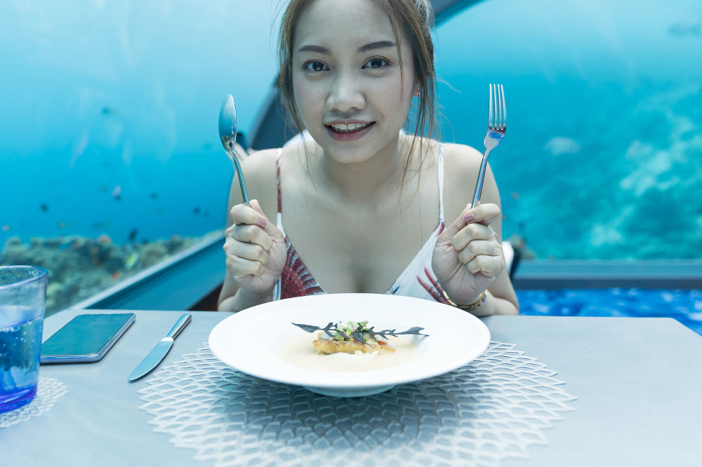 Asian beautiful woman dinner on undersea world background, underwater restaurants in Maldives.