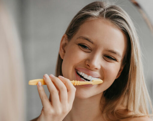 Oral hygiene, healthy teeth and care. Young woman brushing teeth with toothbrush and looking in mirror in bathroom