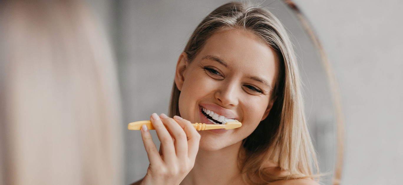 Oral hygiene, healthy teeth and care. Young woman brushing teeth with toothbrush and looking in mirror in bathroom