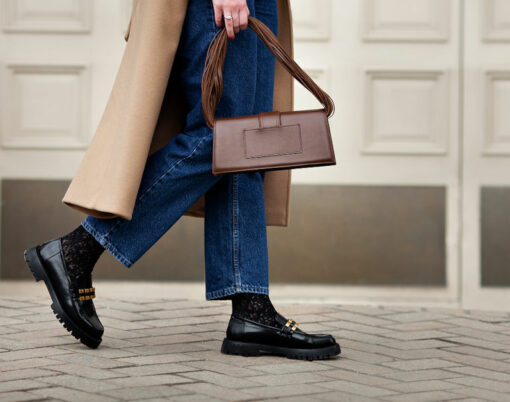 Side view woman walking street in fashionable spring or autumn clothes cashmere coat, jeans, black loafers shoes and handbag. Female model in motion, street style fashion,