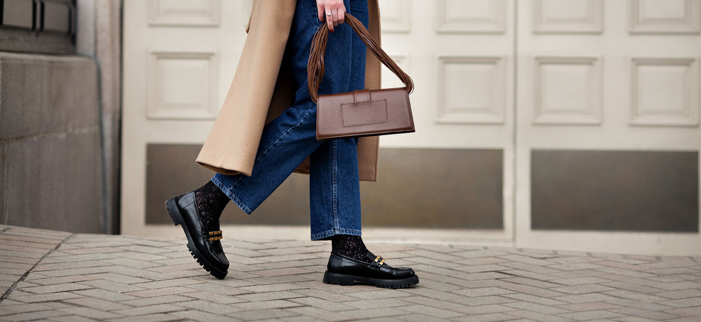 Side view woman walking street in fashionable spring or autumn clothes cashmere coat, jeans, black loafers shoes and handbag. Female model in motion, street style fashion,