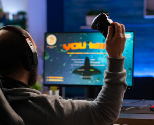 Winner gamer sitting on gaming chair at desk and playing space shooter video games with controller.