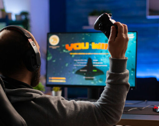 Winner gamer sitting on gaming chair at desk and playing space shooter video games with controller.